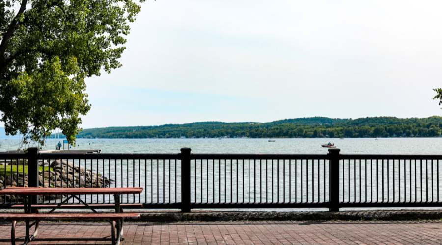 A railing and park table in the foreground overlooking Canandaigua Lake on a cloudy day with a few boats on the water. 